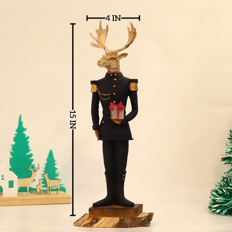 May include: A 15-inch tall figurine of a reindeer wearing a black military uniform with gold accents and holding a small red and white gift box. The reindeer has a gold chain around its neck and a gold button on its jacket. The figurine is standing on a wooden base.