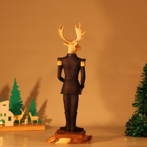May include: A wooden figurine of a moose wearing a black military uniform with gold trim. The moose is standing on a wooden base.