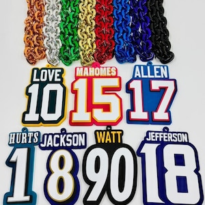 May include: A selection of vibrant chain necklaces and sports-themed pendants. The necklaces are in shades of copper, silver, green, gold, red, blue, and black. The pendants display player names and numbers.