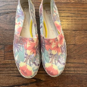 May include: A pair of Anne Klein Flex espadrille flats with a floral pattern in shades of pink, yellow, and blue. The shoes have a yellow interior and a woven sole. The brand name is visible on the side.