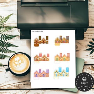 May include: A printed sheet with six miniature gingerbread house designs, each with unique color schemes and architectural details. The text "mini gingerbread" is printed at the top. A printer, a cup of coffee, and a "Print at Home" sticker are also visible.