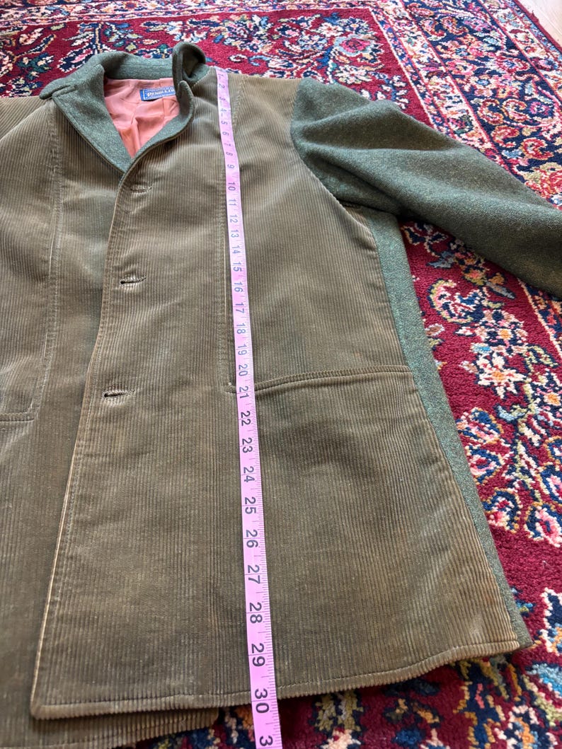 K&ouml;nnte beinhalten: Eine olivgr&uuml;ne Cordjacke mit einem Kragen und &Auml;rmeln aus gr&uuml;nem Wollstoff. Die Jacke hat einen Dreiknopfverschluss und eine Tasche. Die L&auml;nge der Jacke betr&auml;gt ca. 76 cm.