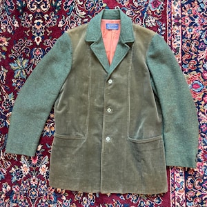 K&ouml;nnte beinhalten: Eine olivgr&uuml;ne Cordjacke mit kontrastierenden gr&uuml;nen Woll&auml;rmeln und Kragen. Die Jacke hat einen Dreiknopfverschluss, zwei Vordertaschen und ein pfirsichfarbenes Futter. Das Pendleton-Etikett ist am Kragen sichtbar.