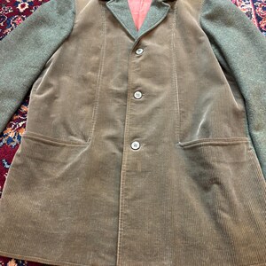 K&ouml;nnte beinhalten: Ein brauner Cord-Blazer mit gr&uuml;nen Woll&auml;rmeln und Kragen. Der Blazer hat drei Kn&ouml;pfe und zwei Vordertaschen. Das Innenfutter ist lachsfarben. Der Blazer ist ein klassischer Stil.