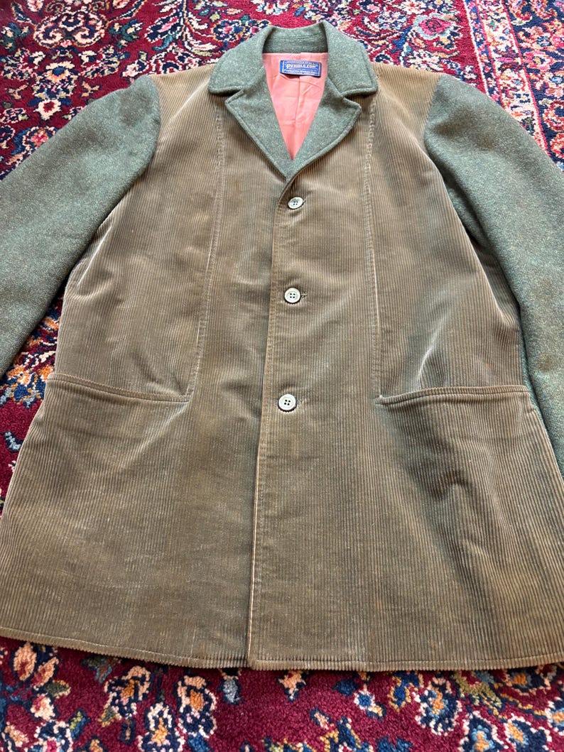 K&ouml;nnte beinhalten: Ein brauner Cord-Blazer mit gr&uuml;nen Woll&auml;rmeln und Kragen. Der Blazer hat drei Kn&ouml;pfe und zwei Vordertaschen. Das Innenfutter ist lachsfarben. Der Blazer ist ein klassischer Stil.