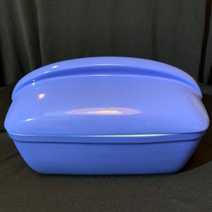 Może przedstawiać: Naczynie do pieczenia z ceramiki w jasnym kolorze liliowym z pokrywką. Pokrywka ma zakrzywiony uchwyt.