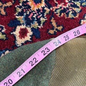 K&ouml;nnte beinhalten: Ein rosa Ma&szlig;band zeigt ein Ma&szlig; von 50,8 bis 66 cm &uuml;ber einem gr&uuml;nen Tweed-Stoff und einem Cordstoff. Die Stoffe sind olivgr&uuml;n und liegen auf einem rot, blau und beige gemusterten Teppich.
