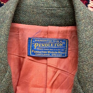 K&ouml;nnte beinhalten: Nahaufnahme eines gr&uuml;nen Tweed-Blazers mit pfirsichfarbenem Futter. Ein blaues Etikett im Inneren zeigt "Pendleton Woolen Mills, Portland, Oregon."