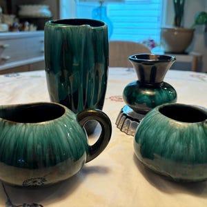 以下が含まれることがあります： ピッチャー、花瓶、小さなボウル2つを含む、緑色の釉薬がかけられた陶器の4つの作品。作品は濃い緑色の釉薬で、薄い緑色の渦巻き模様が施されています。