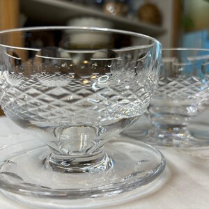 May include: Two clear glass dessert dishes with a diamond pattern. The dishes have a pedestal base and are sitting on a white surface.