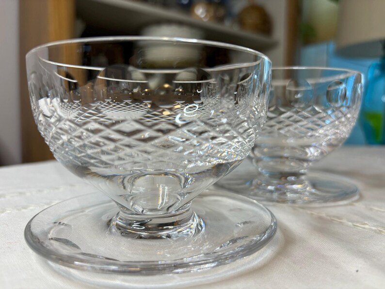 May include: Two clear glass dessert dishes with a diamond pattern. The dishes have a pedestal base and are sitting on a white surface.