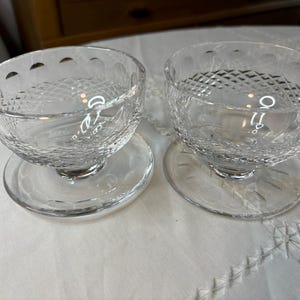 May include: Two clear glass dessert bowls with a diamond pattern on the sides. The bowls are on clear glass saucers.