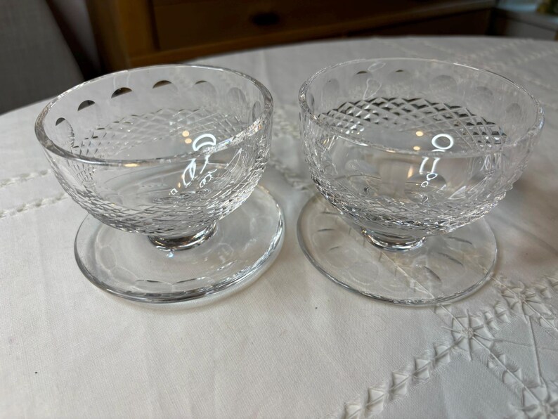 May include: Two clear glass dessert bowls with a diamond pattern on the sides. The bowls are on clear glass saucers.