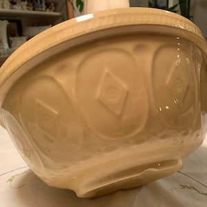 Puede incluir: Un tazón mezclador de cerámica grande de color crema con un patrón de diamante decorativo. El tazón tiene un pequeño astillado en el borde.