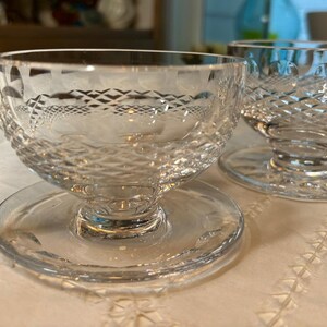 May include: Two clear glass dessert dishes with a diamond pattern. The dishes have a pedestal base and are sitting on a white surface.