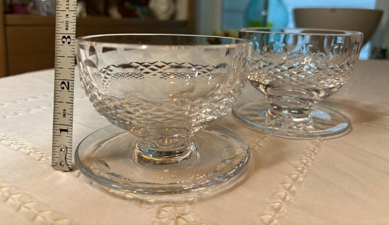 May include: Two clear glass dessert dishes with a diamond pattern. The dishes have a pedestal base and are sitting on a white surface.