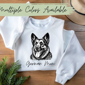 May include: White sweatshirt with a black and white illustration of a German Shepherd dog and the text "German Mom".