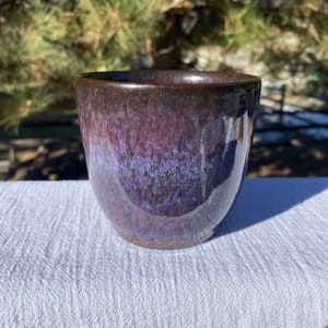May include: A dark purple ceramic mug with a speckled glaze. The mug has a rounded shape and a wide rim.