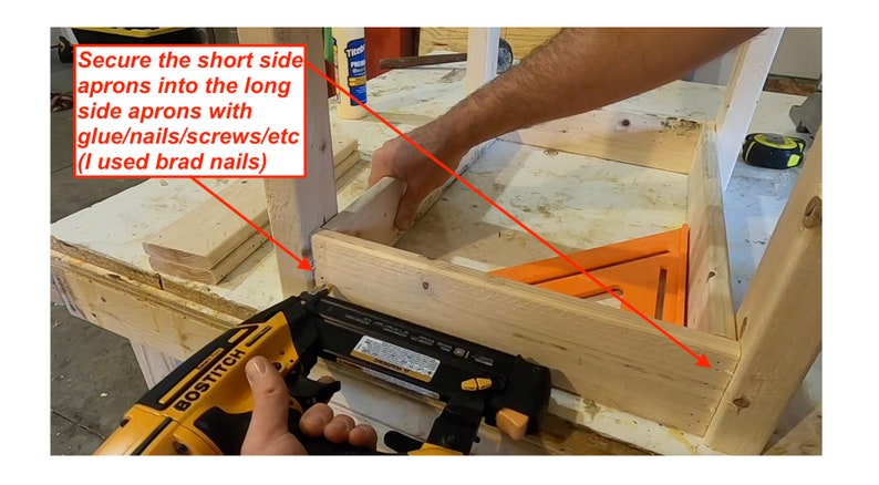 Op de afbeelding: Een persoon gebruikt een spijkerpistool om een ​​houten plank aan een andere houten plank te bevestigen. De planken maken deel uit van een grotere houten constructie. De tekst "Secure the short side aprons into the long side aprons with glue/nails/screws/etc (I used brad nails)" is zichtbaar in de afbeelding.