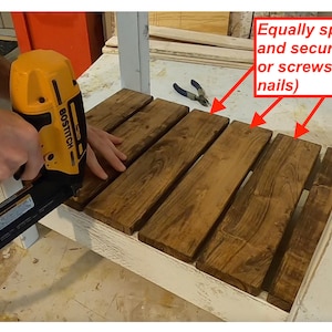 Op de afbeelding: Een persoon gebruikt een spijkerpistool om houten latten aan een wit oppervlak te bevestigen. De tekst in de afbeelding luidt: "Plaats de latten gelijkmatig en bevestig ze met spijkers of schroeven (ik heb brad-spijkers gebruikt)"