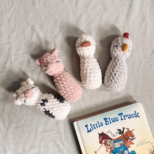 May include: Four crocheted stuffed animals: a pink pig, a white chicken, a gray cow, and a white duck. The animals are lying on a white and gray striped fabric.