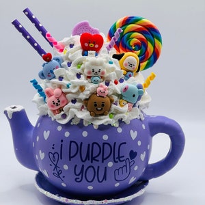 May include: Purple teapot with white polka dots and a white heart design. The teapot is filled with white whipped cream and topped with colorful candy, a lollipop, and various small character figurines. The teapot has the text "i purple you" written on the side.