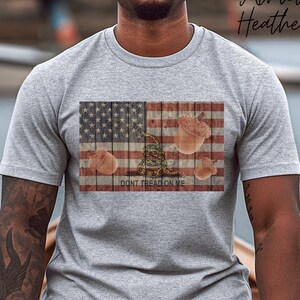May include: Athletic heather gray t-shirt featuring a distressed American flag design with acorns and a coiled snake. The text "DON'T TREAD ON ME" is below the snake. The shirt is a crew neck.