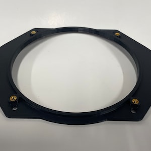 May include: Black plastic speaker adapter ring with four gold screws. The ring is designed to fit a speaker into a larger opening.