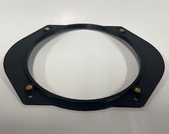 May include: Black plastic speaker adapter ring with four gold screws. The ring is designed to fit a speaker into a larger opening.