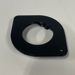 May include: A black, 3D-printed bracket with a circular opening and two mounting holes. The bracket has a curved, asymmetrical shape and appears to be made of plastic. The object is on a white surface.