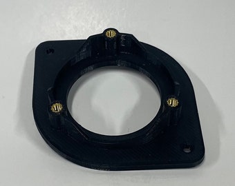 May include: Black, 3D-printed plastic component with a circular opening and three brass-colored threaded inserts. The component has a rectangular base with rounded edges and mounting holes.