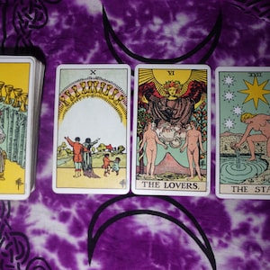 May include: A deck of tarot cards featuring the Nine of Cups, Ten of Cups, The Lovers, and The Star. The cards display colorful illustrations of figures, cups, and celestial bodies with Roman numerals and titles printed at the top or bottom.