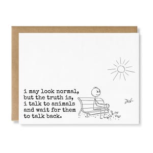 May include: A white greeting card with a black line drawing of a stick figure sitting on a bench feeding birds under a sun. The text reads: i may look normal, but the truth is, i talk to animals and wait for them to talk back. A brown envelope is behind it.