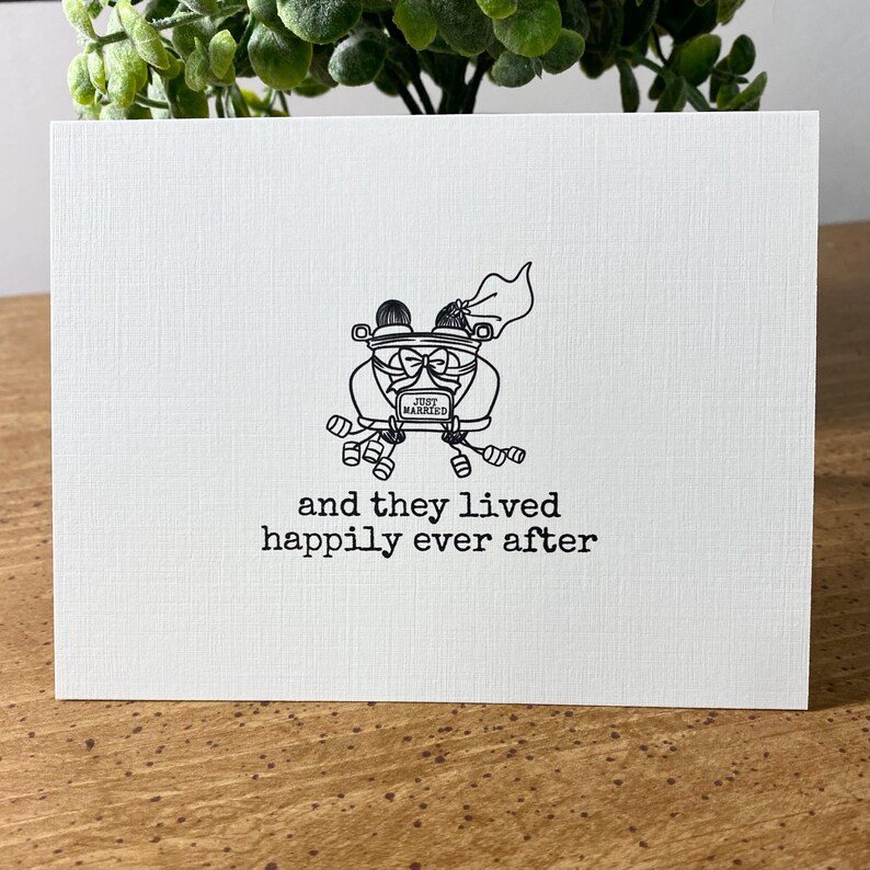 K&ouml;nnte beinhalten: Eine Schwarzwei&szlig;illustration eines Autos mit einem Schild "Just Married" auf der R&uuml;ckseite. Das Auto ist mit Konservendosen verziert und ein Brautpaar sitzt vorne. Der Text "and they lived happily ever after" befindet sich unter dem Auto.