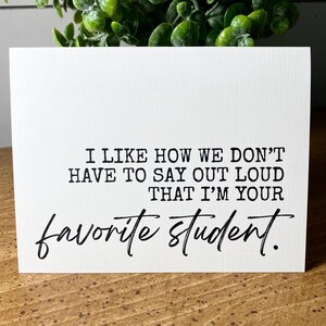 May include: A white card with black text that reads "I like how we don't have to say out loud that I'm your favourite student."