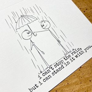 K&ouml;nnte beinhalten: Schwarz-Wei&szlig;-Illustration auf einer wei&szlig;en Karte. Zwei Strichm&auml;nnchen stehen im Regen unter einem Regenschirm. Der Text lautet: "Ich kann den Regen nicht aufhalten, aber ich kann mit dir darin stehen."