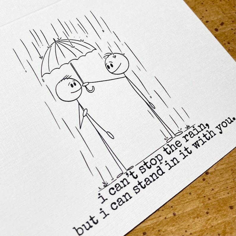 K&ouml;nnte beinhalten: Schwarz-Wei&szlig;-Illustration auf einer wei&szlig;en Karte. Zwei Strichm&auml;nnchen stehen im Regen unter einem Regenschirm. Der Text lautet: "Ich kann den Regen nicht aufhalten, aber ich kann mit dir darin stehen."