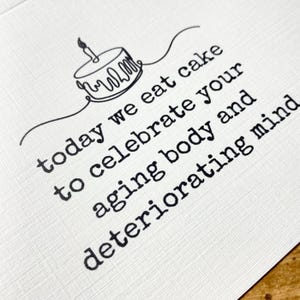 Op de afbeelding: Een verjaardagskaart met een eenvoudige lijntekening van een taart met een kaars. De tekst luidt "vandaag eten we taart om je verouderende lichaam en je verslechterende geest te vieren."