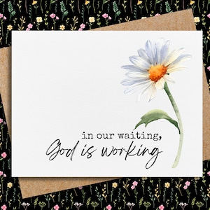May include: A white card with a watercolor illustration of a white daisy with a yellow center. The text "in our waiting, God is working" is written in black cursive.