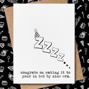 May include: A white greeting card with the word "ZZZZ" in a descending diagonal line, topped with a party hat. The text "congrats on making it to your in bed by nine era" is printed below the ZZZZ.
