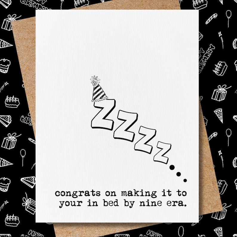May include: A white greeting card with the word "ZZZZ" in a descending diagonal line, topped with a party hat. The text "congrats on making it to your in bed by nine era" is printed below the ZZZZ.