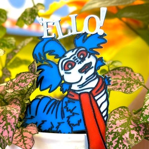 May include: A blue and white 3D printed figurine of a creature with the word "Ello" above it. The creature has a red scarf and a blue and white striped body.