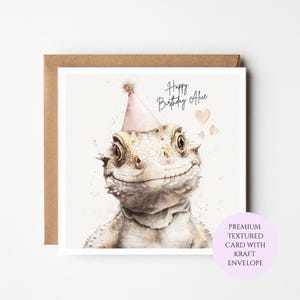 May include: A square greeting card featuring a watercolour illustration of a bearded dragon wearing a light pink party hat. The text reads Happy Birthday Alice, accompanied by three small pink hearts. The card is paired with a brown kraft envelope.