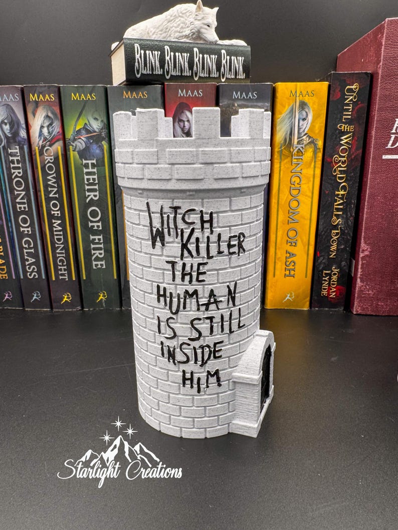 Puede incluir: Un objeto decorativo gris en forma de castillo con el texto "Witch Killer The Human Is Still Inside Him". El art&iacute;culo est&aacute; hecho de un material similar al ladrillo y tiene una peque&ntilde;a puerta arqueada. Libros y una figura de lobo en el fondo.