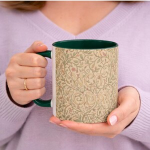 May include: A white ceramic mug with a green handle and interior. The mug features a beige floral pattern with the words "NOT TODAY" in a decorative font. The mug is held by a person wearing a purple jumper.