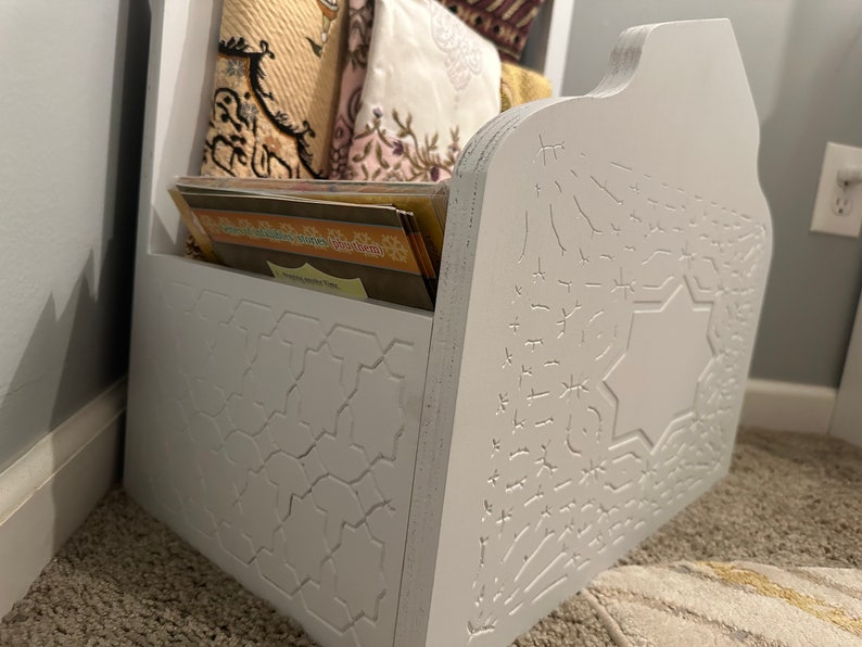 May include: White wooden prayer shelf with intricate carved designs. The shelf has a compartment for storing prayer rugs and books. The shelf is decorated with a star and geometric patterns.