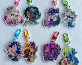 May include: Eight colorful holographic keychains featuring characters from the video game Splatoon. The keychains are made of clear acrylic and feature different characters from the game, including a squid, an octopus, and a jellyfish. Each keychain has a different colored metal clasp.