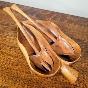 Puede incluir: Un bol de ensalada de madera con dos utensilios para servir. El bol tiene forma de hoja y tiene dos compartimentos separados. Los utensilios son un tenedor y una cuchara.