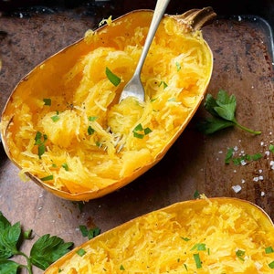 May include: Two halves of a cooked spaghetti squash, with the flesh pulled apart into strands. The squash is seasoned with salt, pepper, and fresh parsley.