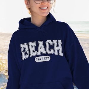 May include: A navy blue hoodie with a white graphic that says "Beach Therapy" with a palm tree design.